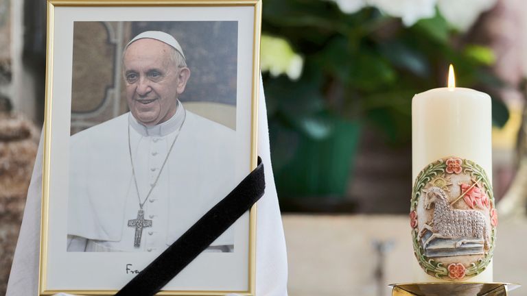 A candle stands next to a photograph of Pope Francis placed at Saint Magdalena Catholic church in Altoetting, Germany, Monday, April 21, 2025. (AP Photo/Matthias Schrader)
