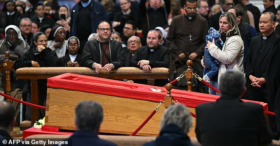Faithful react next to the coffin as they pay their respects to late Pope Francis inside St Peter's Basilica in The Vatican, on April 24, 2025. The Vatican said on April 24, 2025, that nearly 50,000 people had so far paid their respects to Pope Francis, whose body is lying in state at St Peter's Basilica for three days before his funeral. (Photo by Andreas SOLARO / AFP) (Photo by ANDREAS SOLARO/AFP via Getty Images)