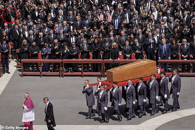 A wider shot of the Deputy Speaker of the Ugandan Government taking the image as bearers carry the religious leader's coffin
