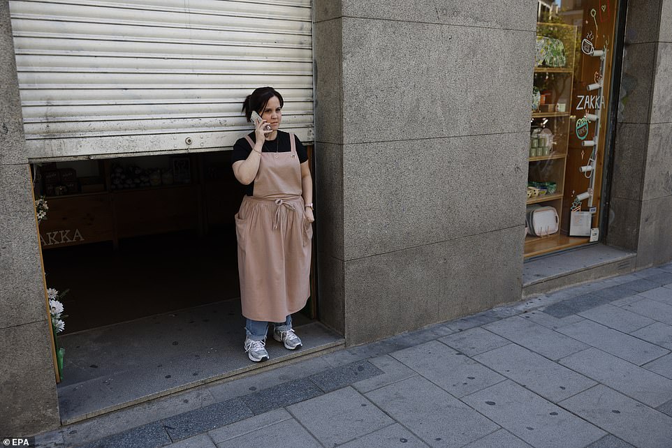 A worker tries unsuccessfully to use her mobile outside a shop after a blackout hit Madrid
