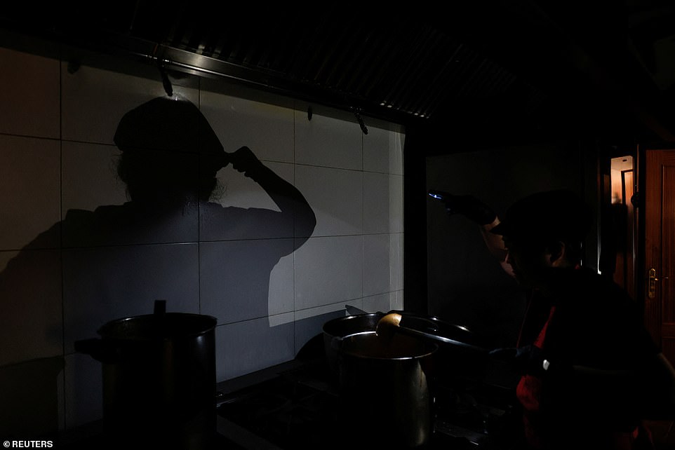 A cook at a takeaway restaurant works in a dark kitchen with the aid of phone's flashlight during a power outage in Madrid