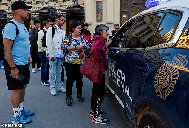 People stand next to a police car, as a power outage hits large parts of Spain, in Valencia, Spain, April 28, 2025