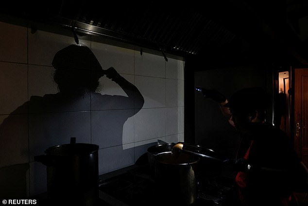 A cook at a takeaway restaurant works in a dark kitchen with the aid of phone's flashlight during a power outage in Madrid