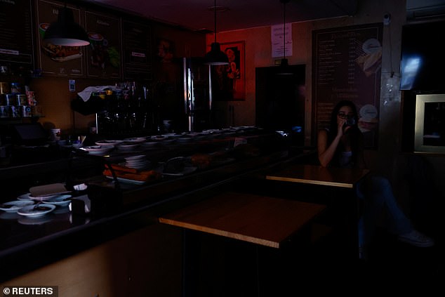 A woman has a drink in the dark inside a bar with outside light coming in through the door during a nationwide power outage in Madrid, Spain, April 28, 2025