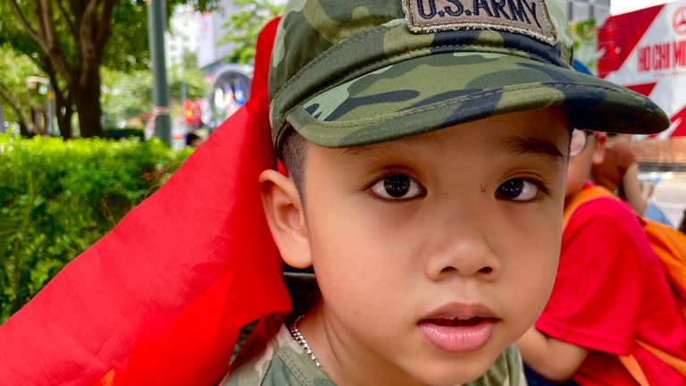 A boy with a Vietnamese flag while wearing a US army hat