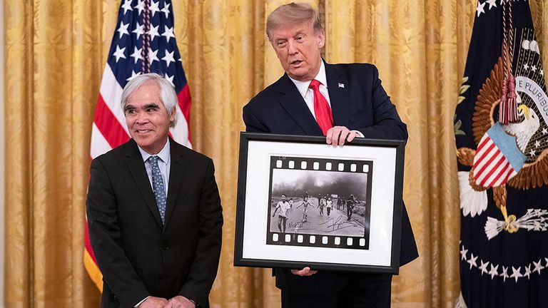 Donald Trump holds the famous photograph while standing with Nick Ut