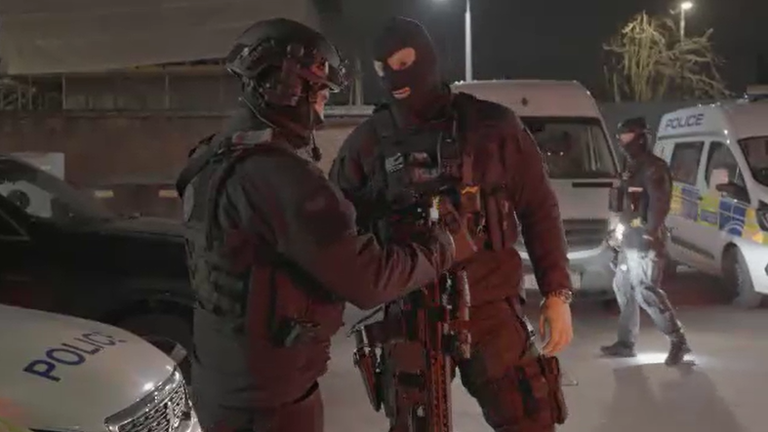 Armed police officers ready their weapons before a dawn raid