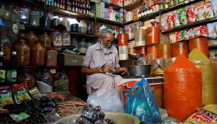 A shopkeeper uses a calculator while selling spices and grocery items along a shop in Karachi. — Reuters/File