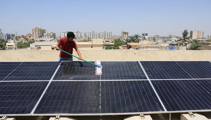 Syed Fahim Ali, 30, uses a wiper to clean the solar panels installed on the roof top of his home, in Karachi, April 5, 2025. — Reuters
