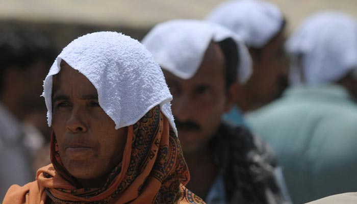 Relatives of heatstroke victims, their heads covered with wet towels, wait outside a hospital during a heatwave in Karachi on June 29, 2015. — AFP/File