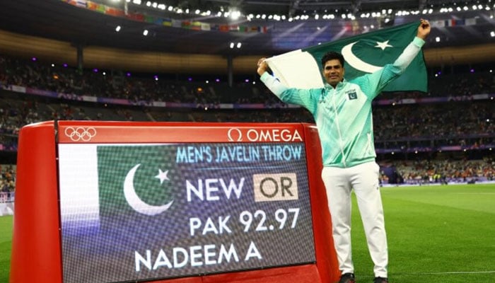 Arshad Nadeem celebrates with his national flag after winning gold as he stands next to a screen displaying his new Paris 2024 Olympic record in France on August 8, 2024. — Reuters