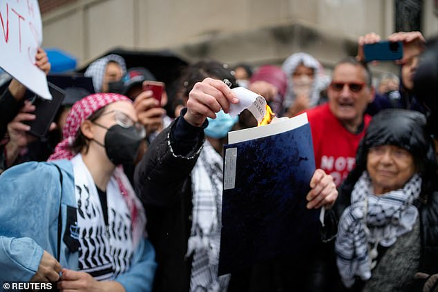 Pictured: A person setting fire to their diploma as others watch on