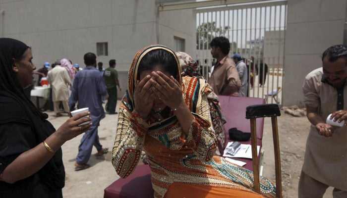 A woman wets her face to cool off, while sitting outside Jinnah Postgraduate Medical Centre during intense hot weather in Karachi, Pakistan, June 23, 2015 — Reuters