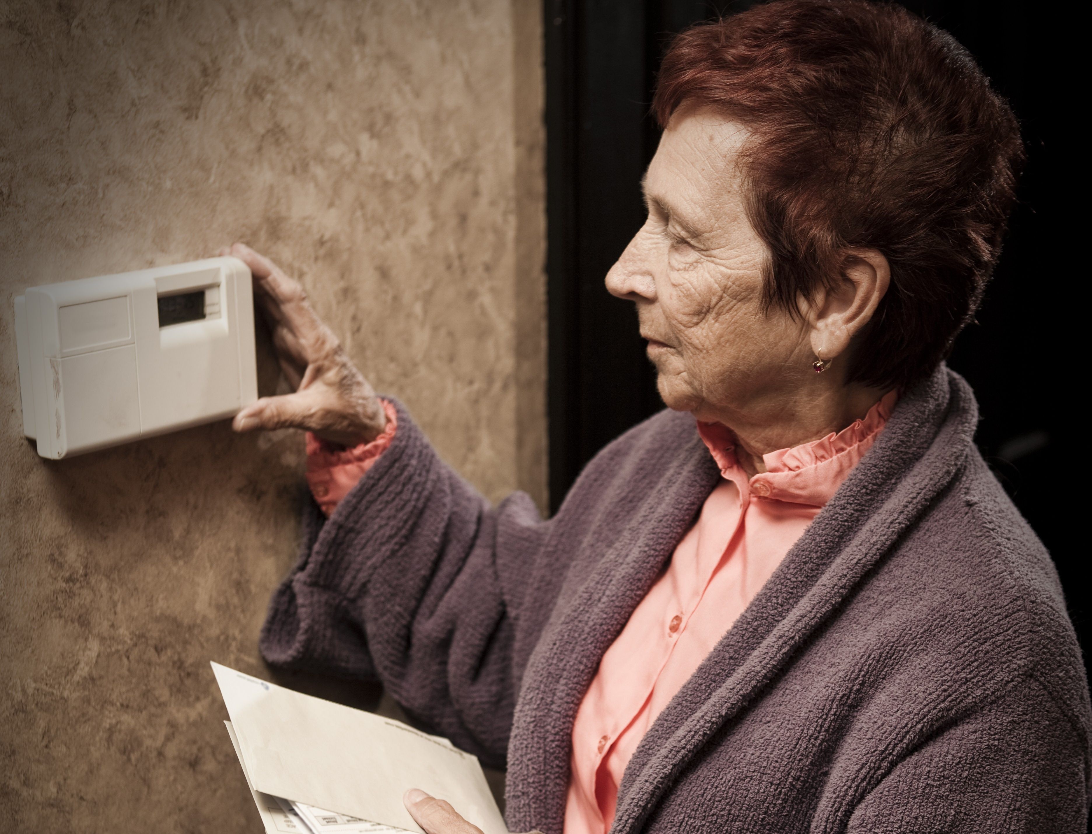 Pensioner with energy bills looks at thermostat