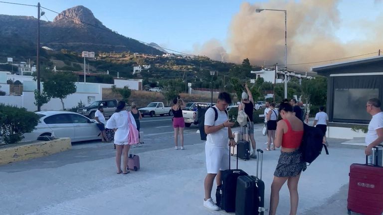 People stand with their luggage as smoke billows from a wildfire, in Ferma, Crete. Pic: Reuters/d_morice
