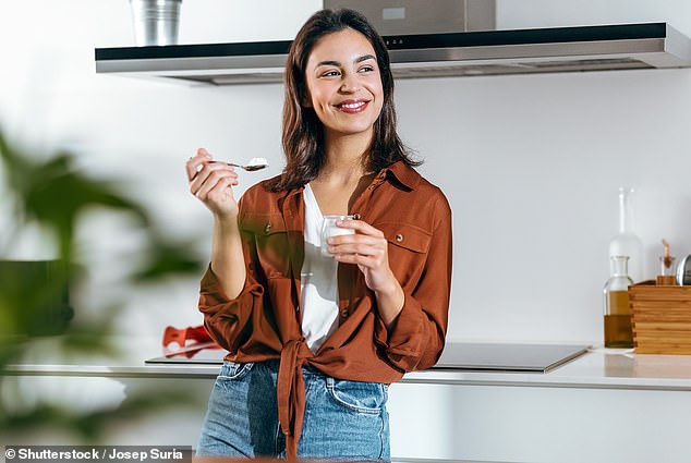 A woman is shown above eating a yogurt (stock photo)