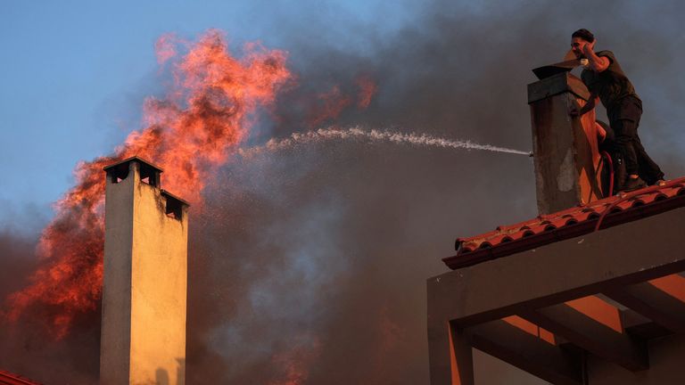 Locals try to extinguish flames rising from a burning house, as a wildfire burns in the village of Kryoneri, near Athens, Greece, July 26, 2