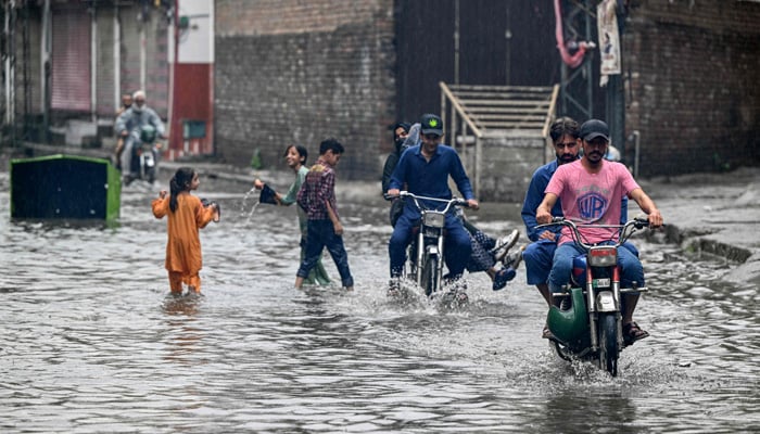 Commuters wade through while children play in a flooded street amidst heavy monsoon rains in Rawalpindi on July 17, 2025. — AFP