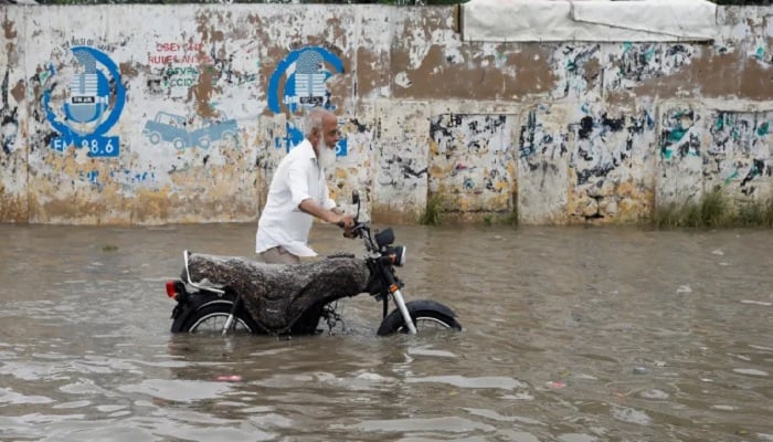 A man pushes his bike as he wades through a flooded road in Karachi. —Reuters/File