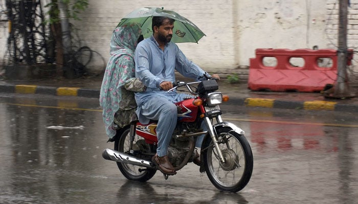 A man and woman travel on a motorcycle under the cover of umbrella to protect from rain, in Lahore on June 26, 2025. — Online