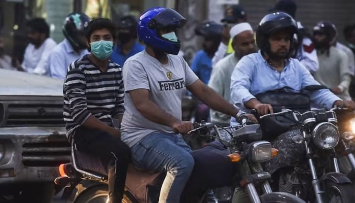 Motorists riding motorbikes along a street wearing facemasks. — AFP/File