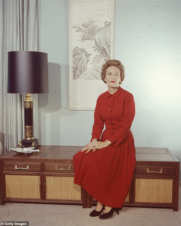 First Lady Pat Nixon, wife of American President Richard Nixon, wearing a red dress and sitting on a cabinet, circa 1970s