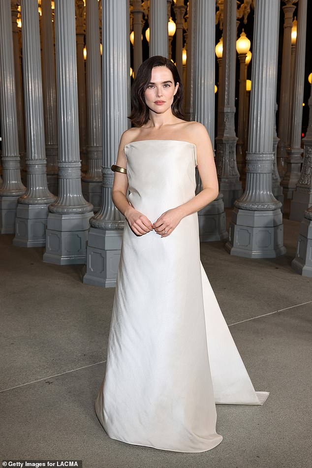 Zoey Deutch looked glamorous in a white off-the-shoulder gown with a golden cuff on her arm