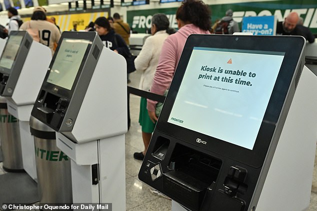 An inoperable kiosk is seen at Frontier's check-in gate at Hartsfield-Jackson Airport in Atlanta on Friday as travelers queue to speak with an agent