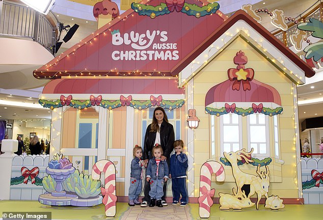 Dani cut a trendy figure in a brown leather jacket worn over a white T-shirt and grey faded jeans as she posed with her children in front of the Bluey display