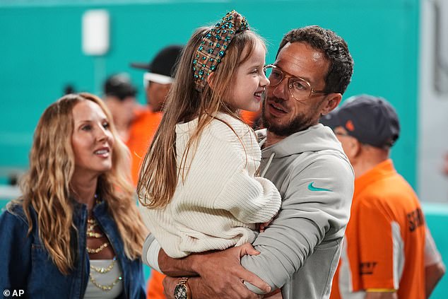 Dolphins coach Mike McDaniel, right, holds daughter, Ayla June, center, on the sidelines as his wife, Katie Hemstalk, left, stands nearby. McDaniel has been sober since January of 2016