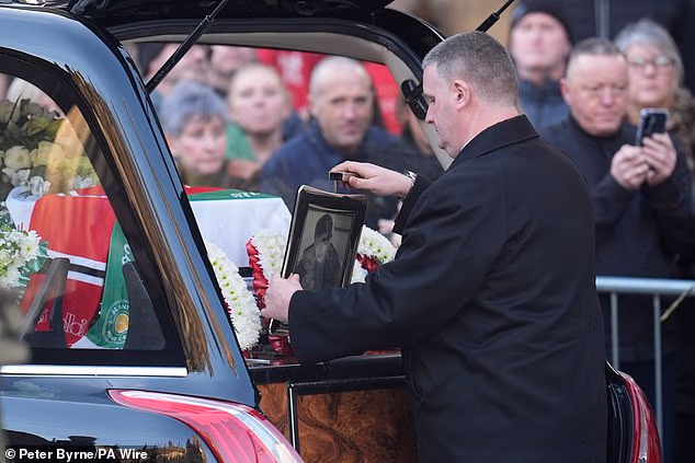 A funeral director places a framed photo of Mani beside his coffin in the rear of the hearse as it arrives for his funeral