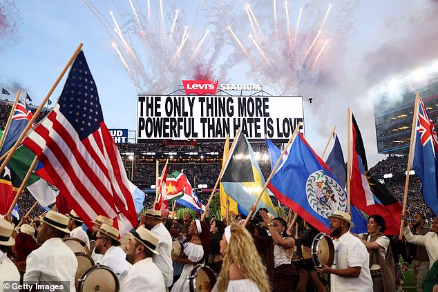 Behind him, an electronic billboard reading 'The only thing more powerful than hate is love' shone out above the field