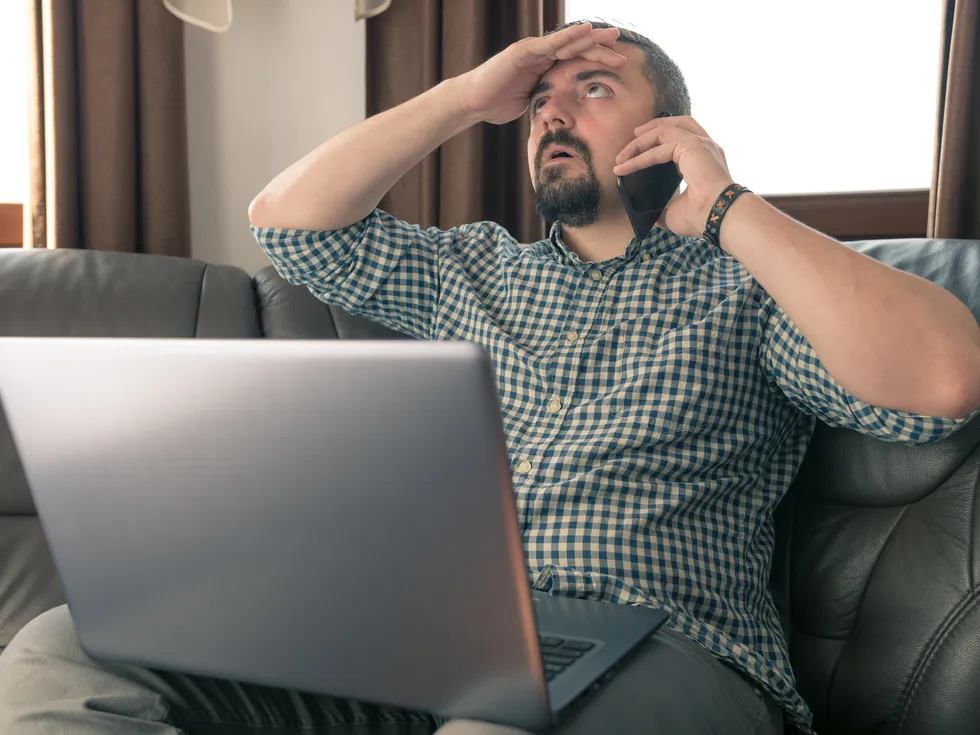 Man annoyed while speaking on the phone and using his laptop