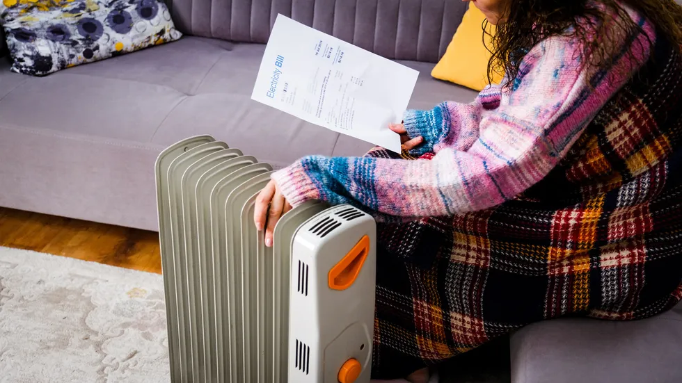 Person sits by heater with electricity bill during very cold weather in pictures