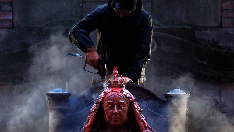 A man uses a power hose to remove red paint from the statue of Queen Victoria. Pic: PA