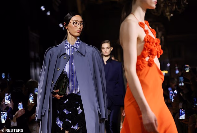 A model is seen presenting a Victoria Beckham creation featuring a striped shirt and trench coat