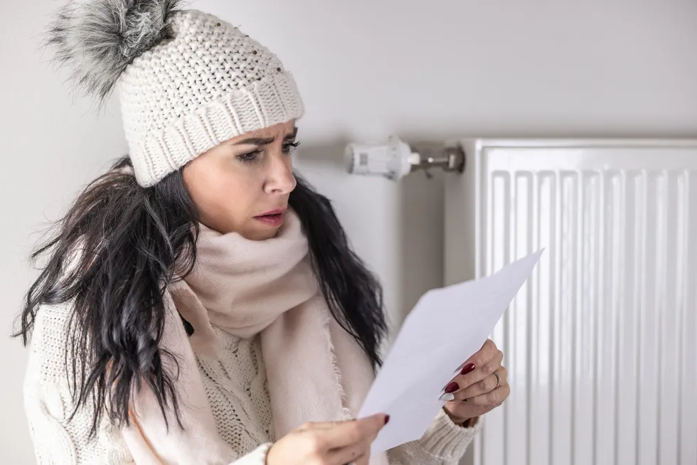Woman in jumper and hat inside looking worried at energy bill